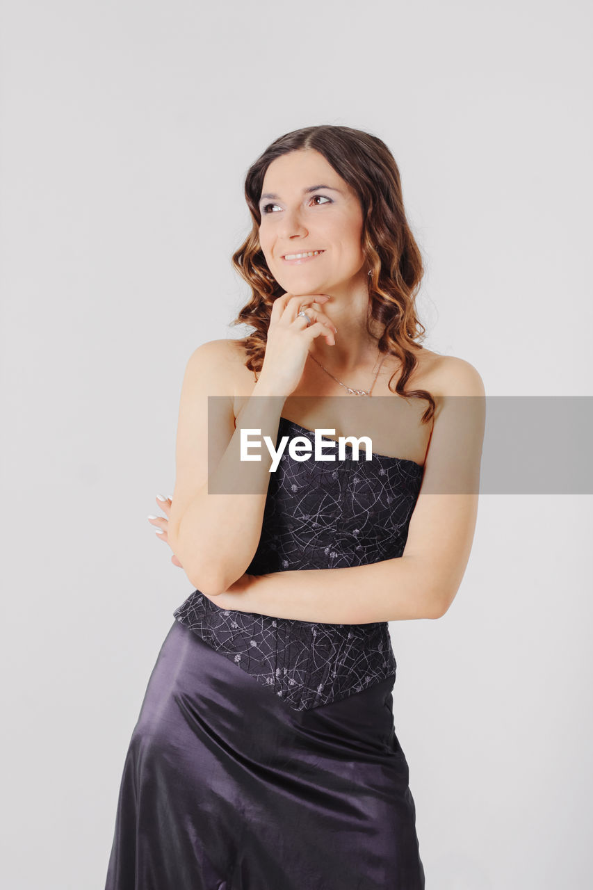 Smiling thoughtful woman with hand on chin standing against white background