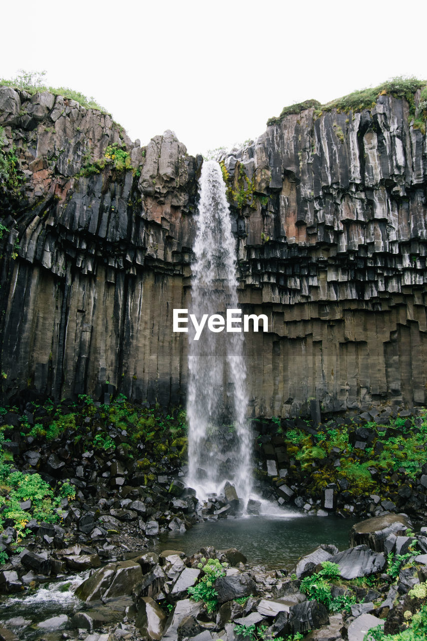 Low angle view of waterfall against clear sky