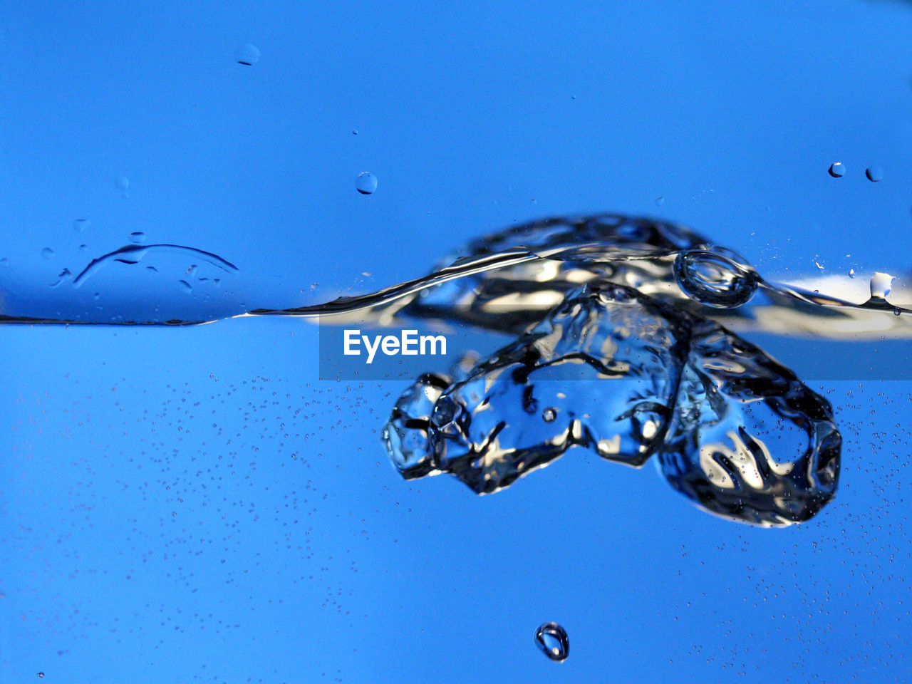 CLOSE-UP OF DROP SPLASHING ON BLUE WATER AGAINST SKY