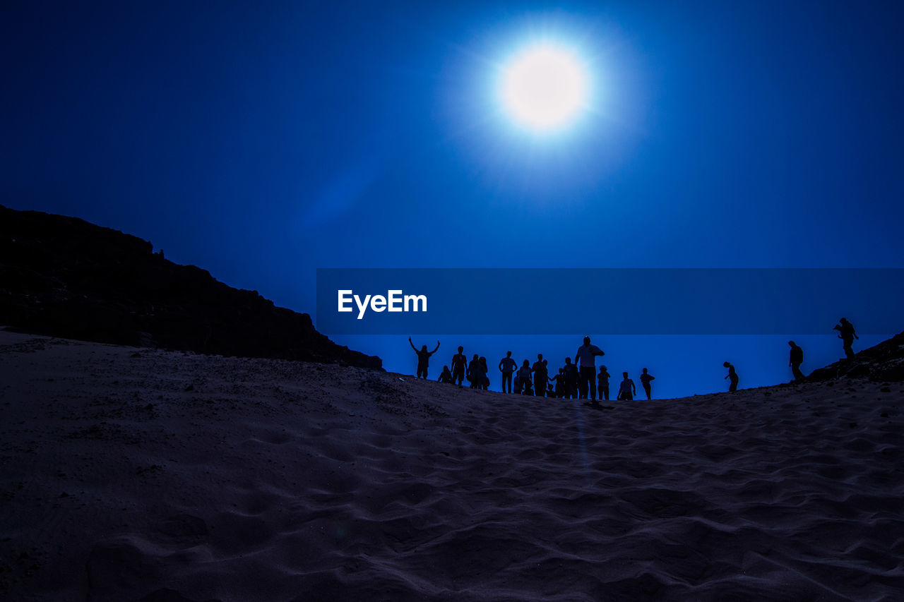 Silhouette people standing at beach against blue sky