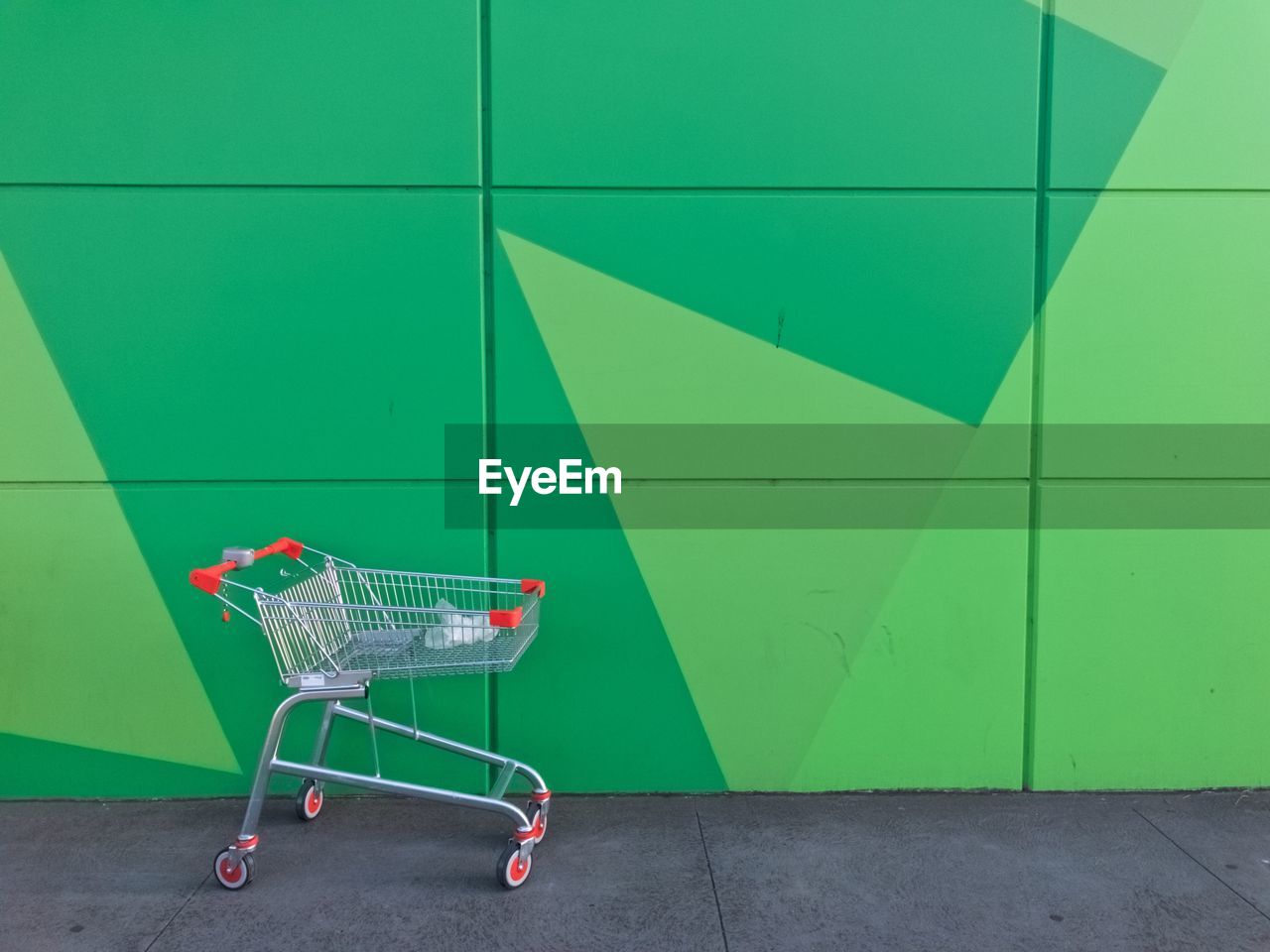 Shopping cart against green wall