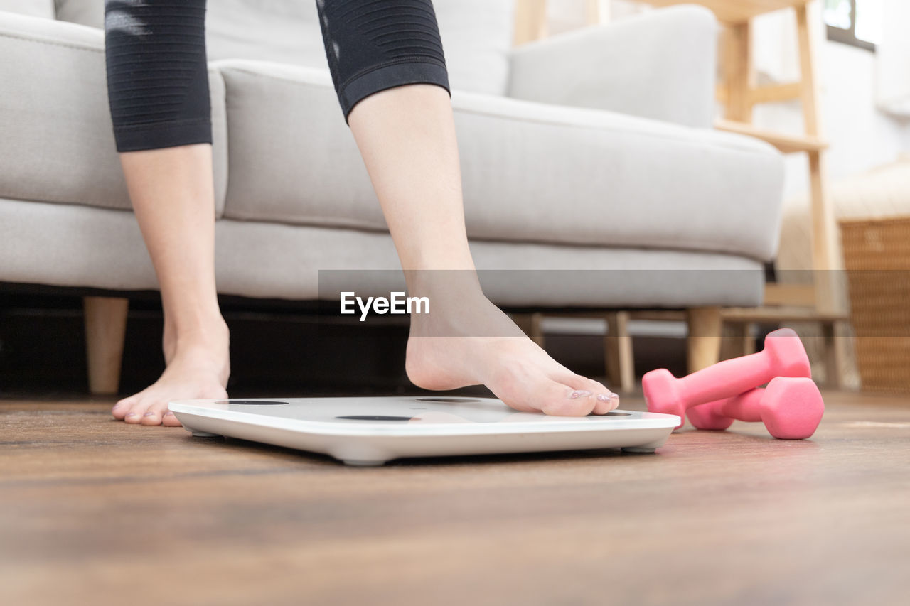 low section of woman using mobile phone while sitting on sofa at home