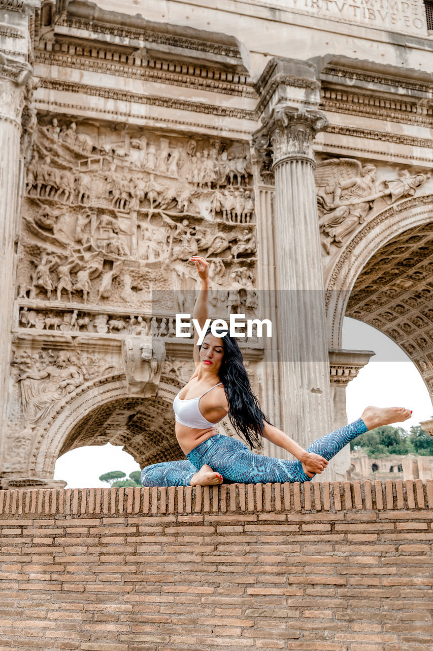 Full length of woman with arms raised in front of historic building