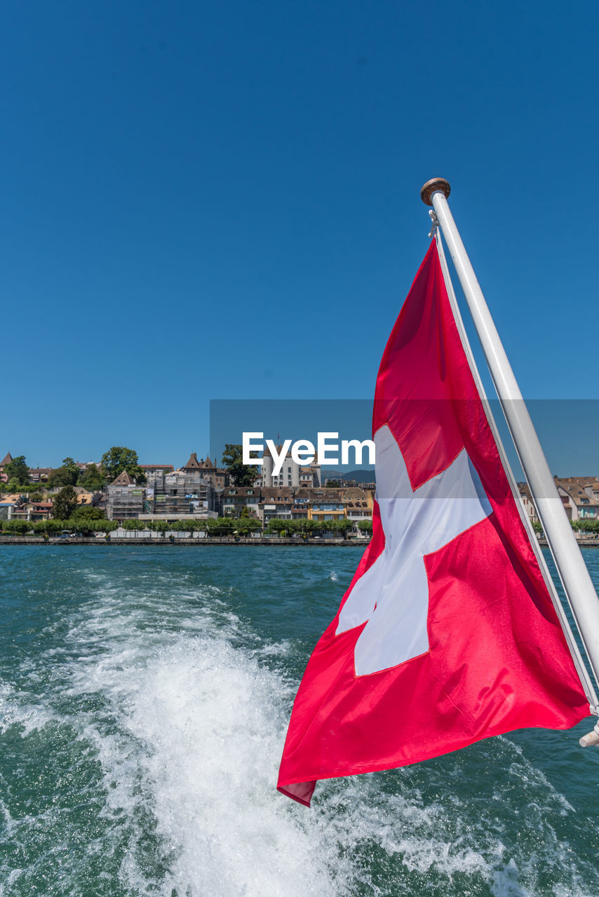 Vertical photo of the swiss flag fluttering in the wind from a boat in the wake of lake geneva.
