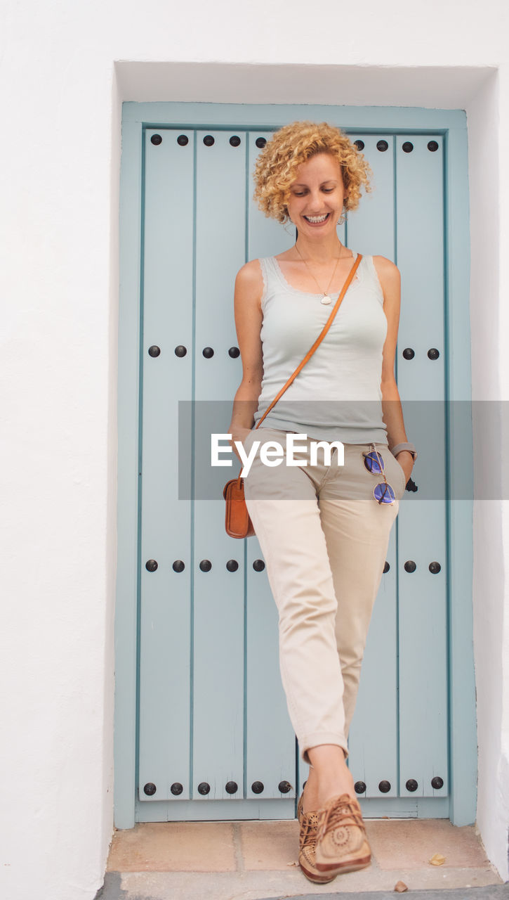 Portrait of smiling young woman standing against door