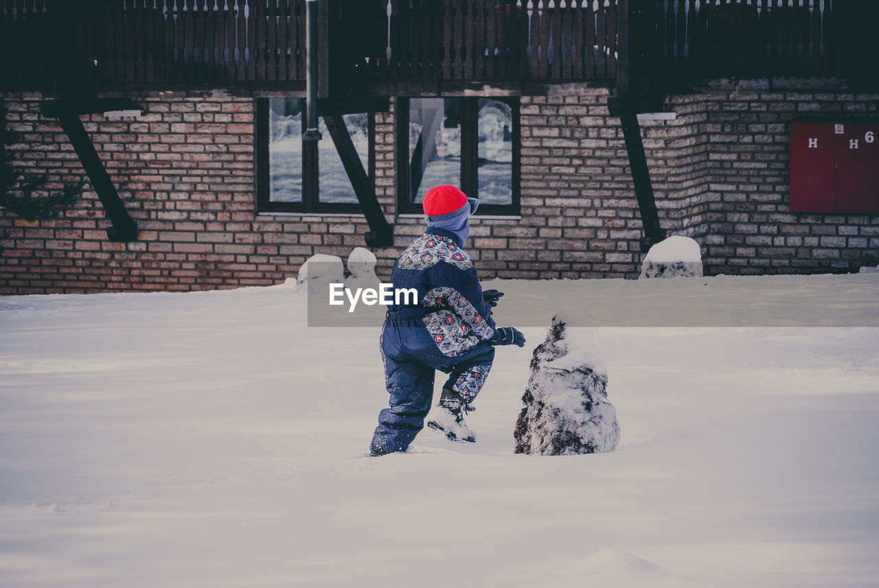 Rear view of boy playing on snow covered yard during winter