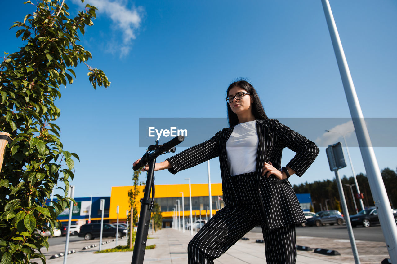 Low angle view of woman with push scooter standing against blue sky