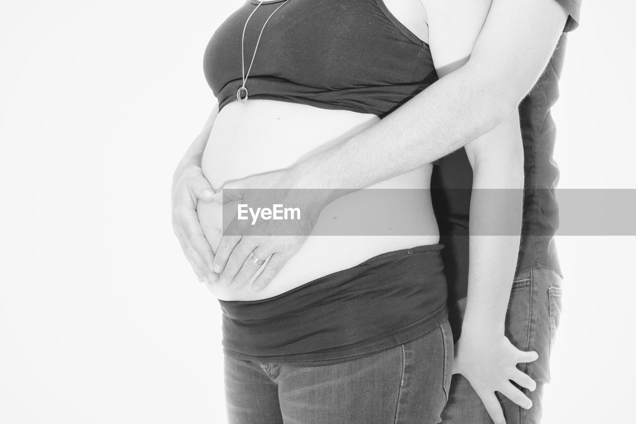 MIDSECTION OF WOMAN WITH ARMS RAISED AGAINST WHITE BACKGROUND