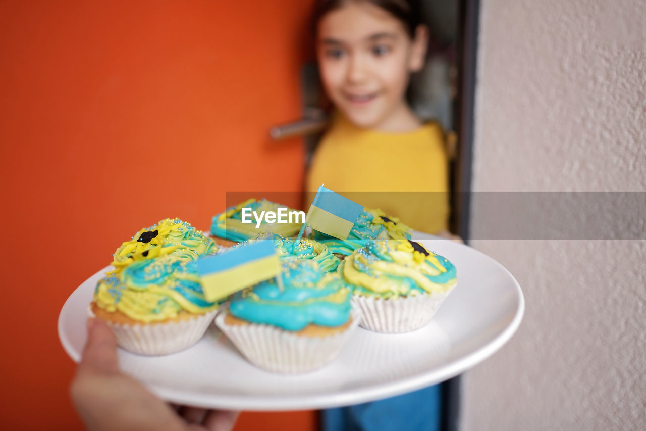 Ukrainian girl for whom neighbors brought cupcakes with cream in yellow and blue colors for brunch