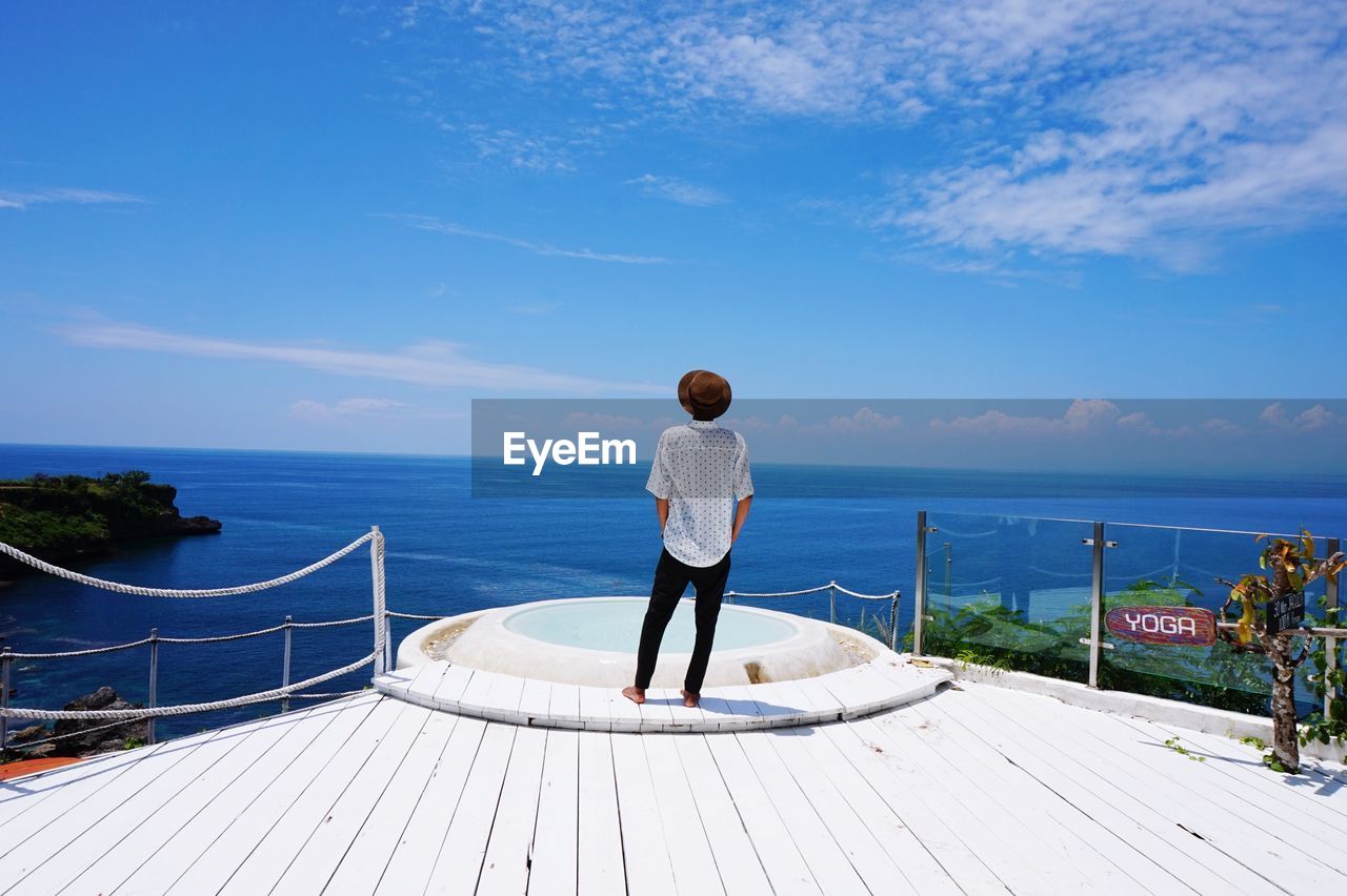 Rear view of man standing on wooden deck at resort against sea