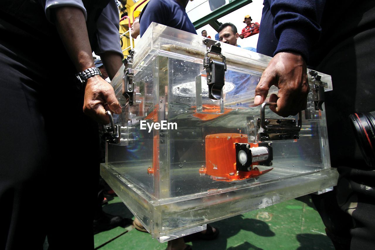 Cropped image of manual workers holding glass container in factory