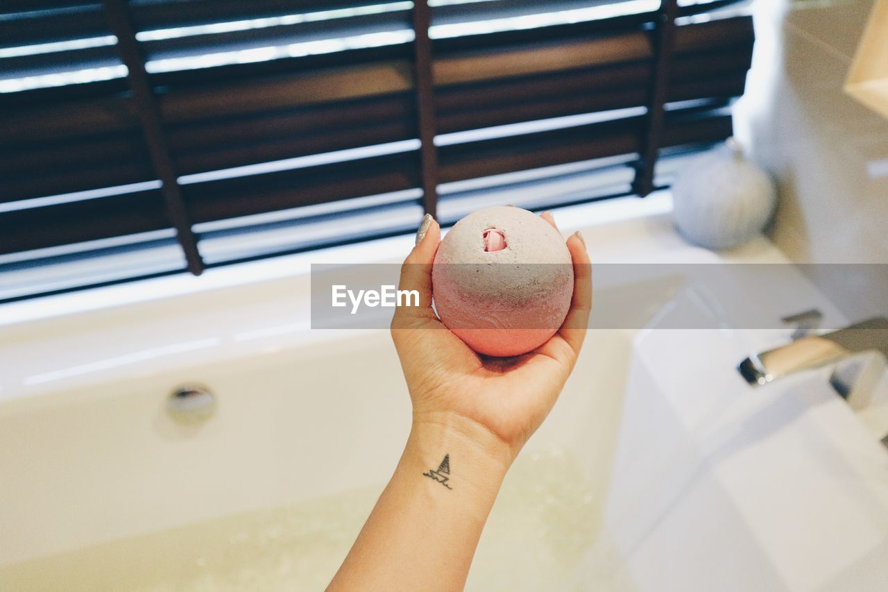 Cropped hand of woman holding object over bathtub at home