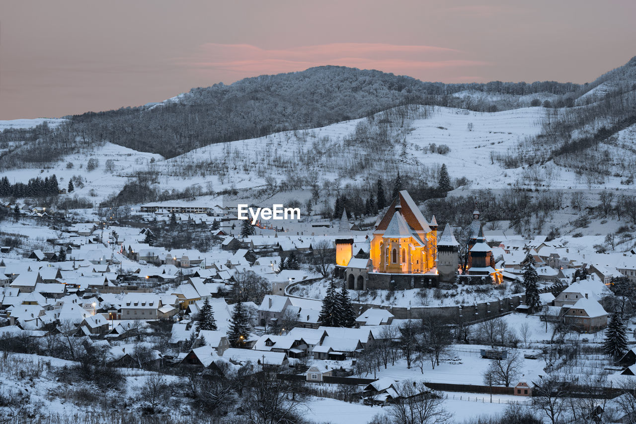 Snow covered houses and fortified church against  mountain and sky during winter