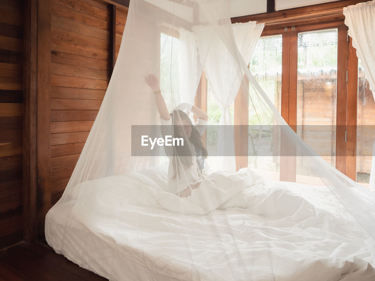 Woman stretching in bed after wake up, happy greets new day with warm sunlight.