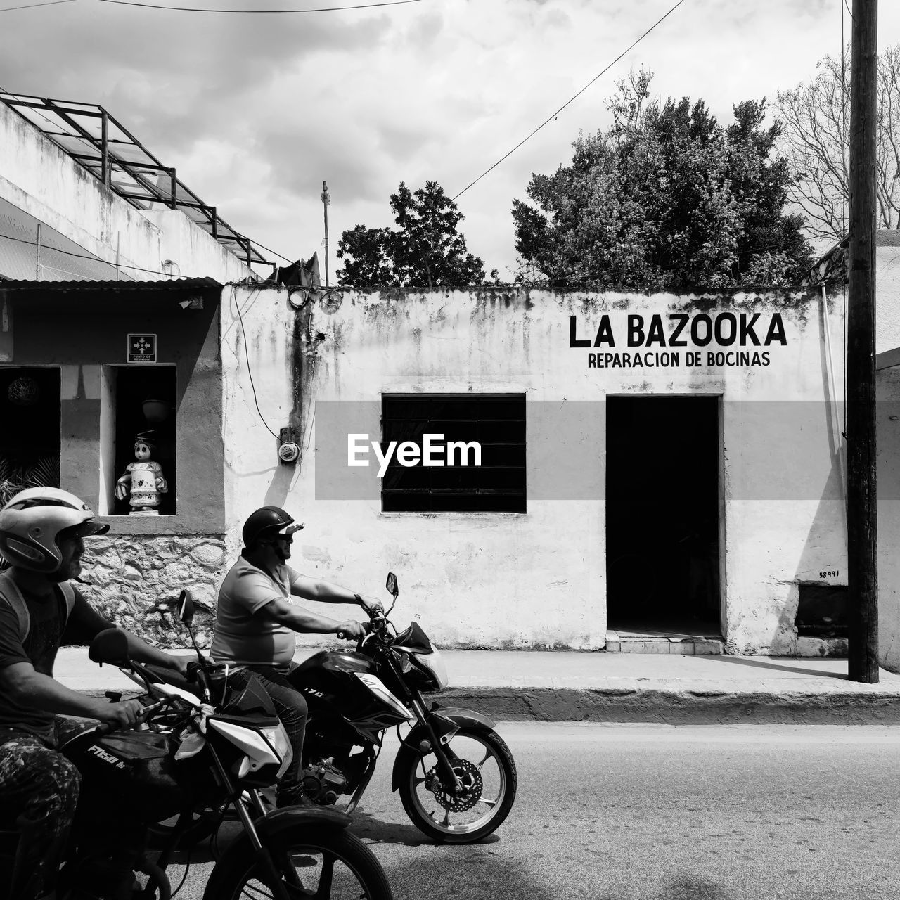 transportation, architecture, black and white, black, monochrome, street, building exterior, mode of transportation, road, built structure, monochrome photography, city, motorcycle, white, men, infrastructure, land vehicle, adult, day, building, full length, vehicle, text, nature, outdoors, communication, person, bicycle, tree, lifestyles, cloud, sky, sign, urban area