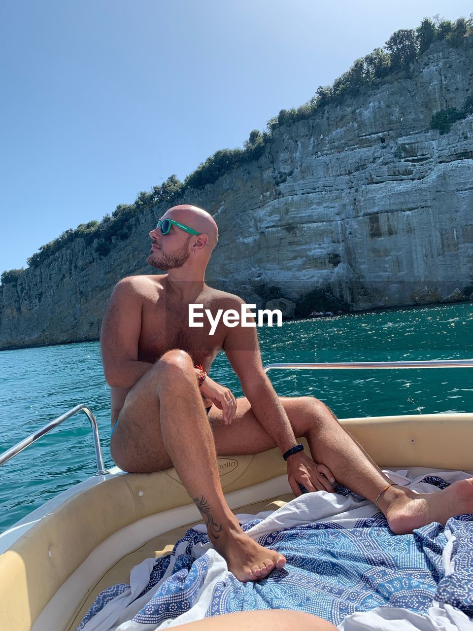 Full length of shirtless man sitting in sea against sky