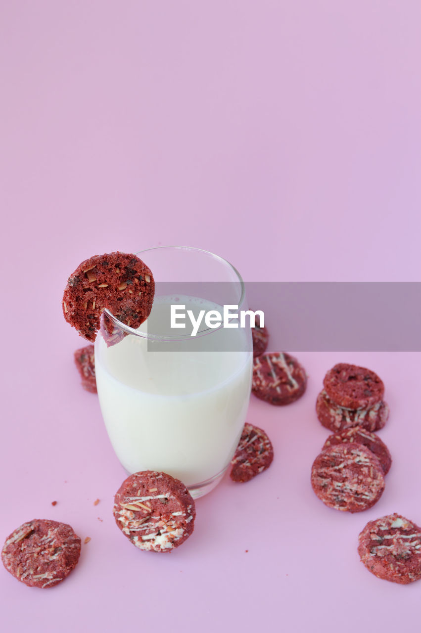 Red cookie on glass of milk with many others spread out in pink background