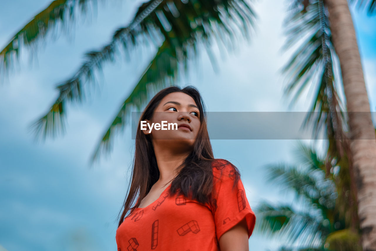 Young woman looking away against sky