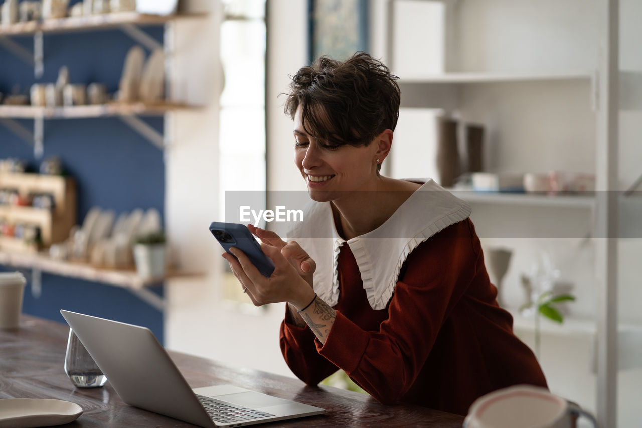 Happy successful woman small business owner chatting on mobile phone while working in pottery shop