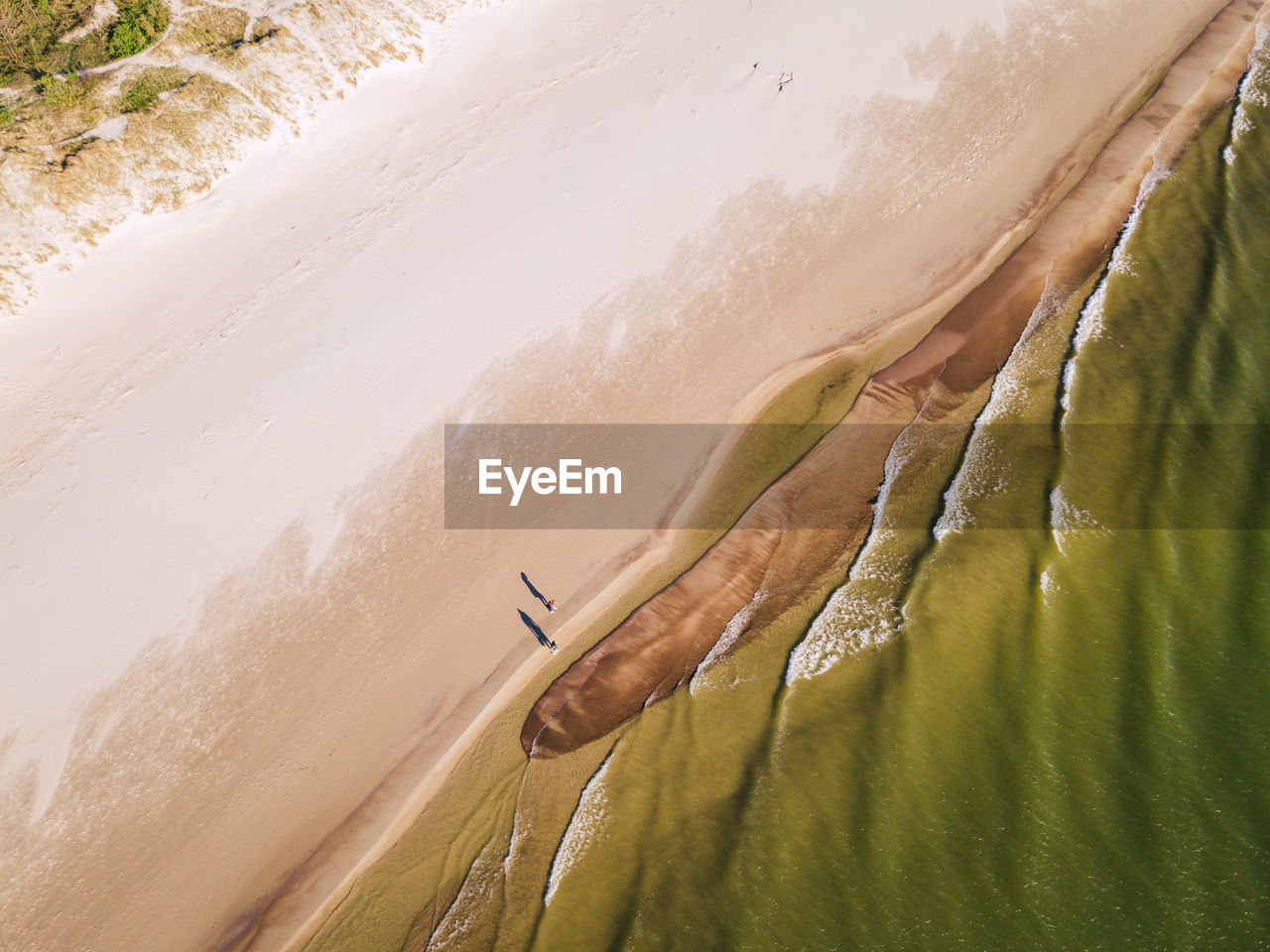 Couple walking on the sandy beach from above. shadows and the sea waves. bird drone view.