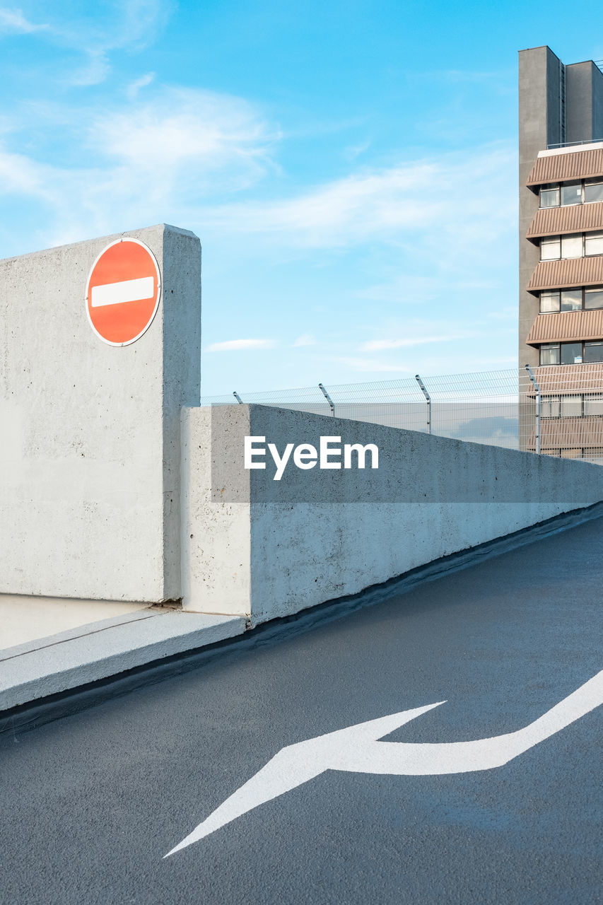 Directional arrow and stop sign against blue sky,  on the roof of a parking lot.