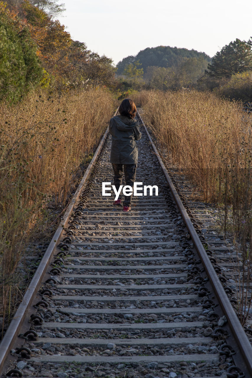 Rear view of woman walking on railroad track