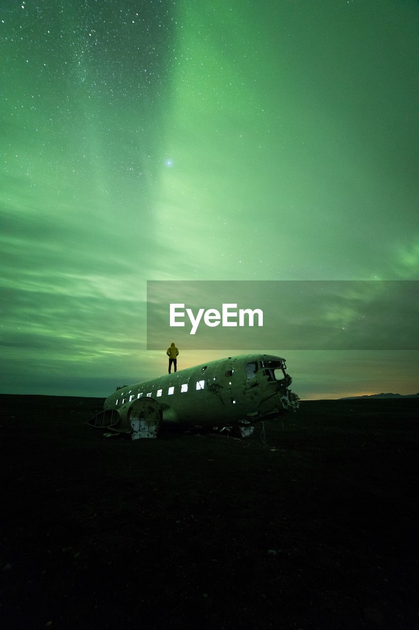 Man standing on dc-3 airplane against aurora borealis at night