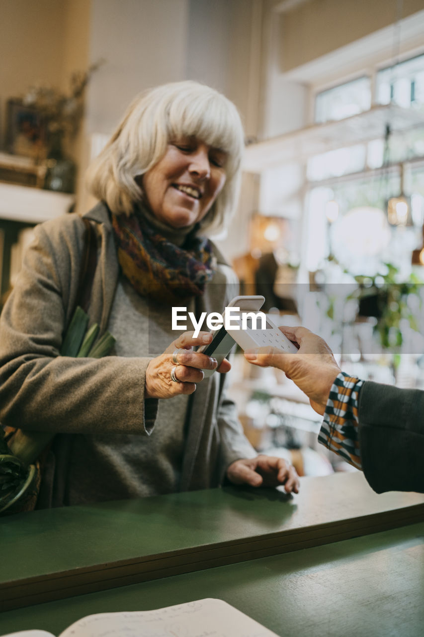 Senior woman paying via tap to pay method while doing shopping at store