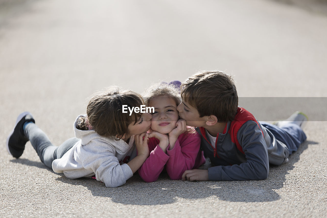 Siblings kissing sister while lying down on road