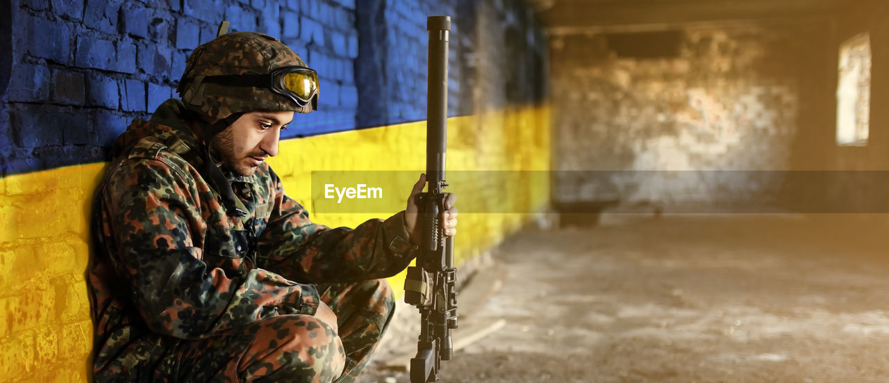 Military soldier on the background of the flag of ukraine. the flag of ukraine is painted on a brick