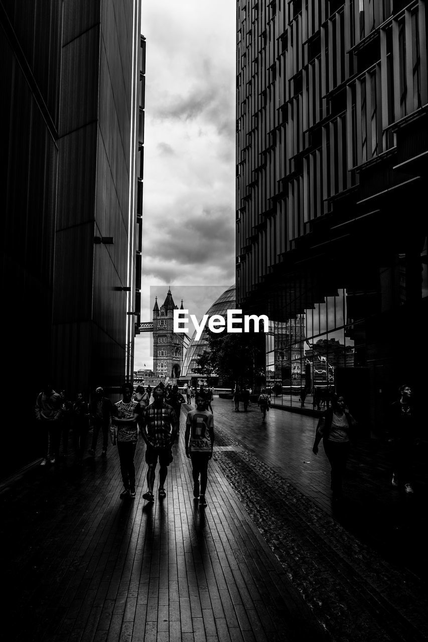 PEOPLE WALKING ON STREET AMIDST BUILDINGS IN CITY AGAINST SKY