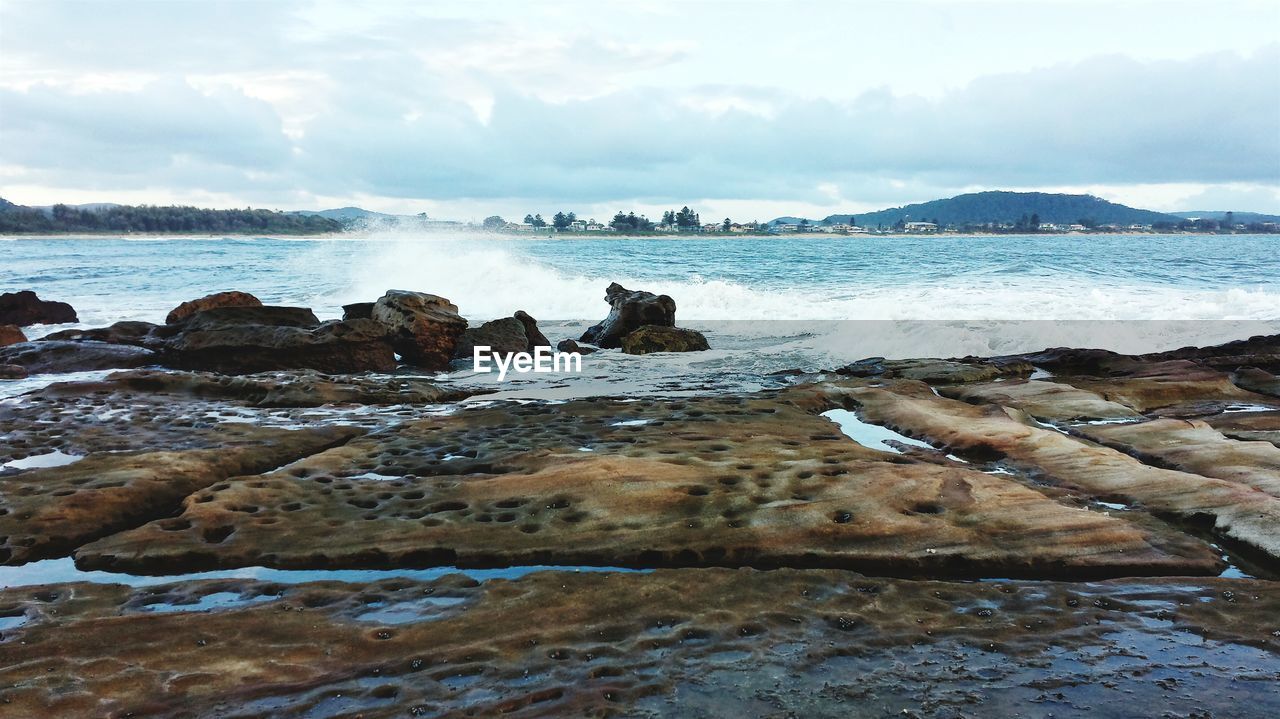 View of rocks at beach against cloudy sky