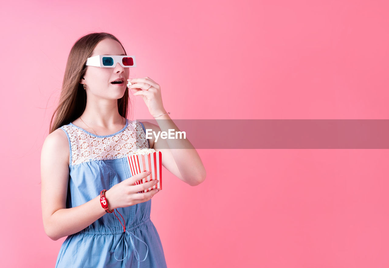 YOUNG WOMAN WEARING SUNGLASSES AGAINST PINK BACKGROUND