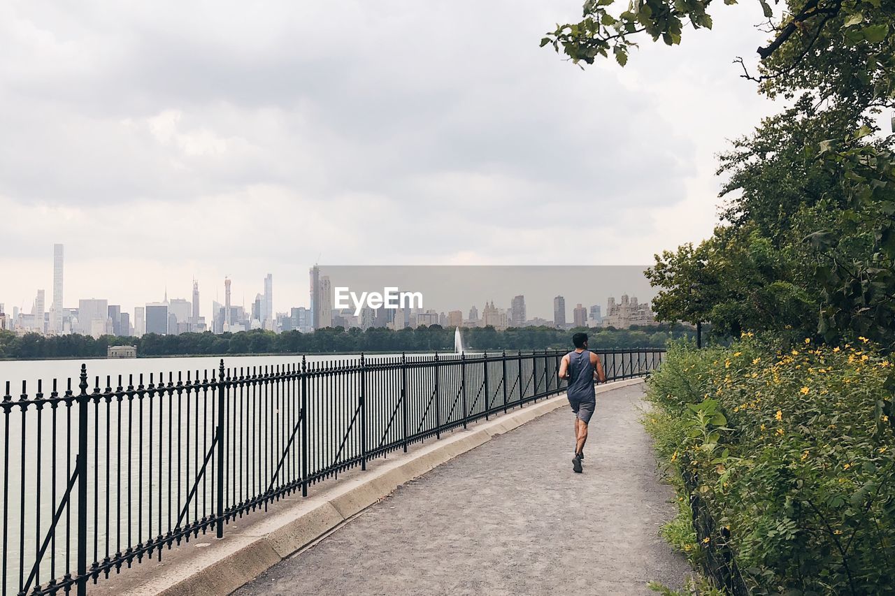 Rear view of man jogging on promenade in city