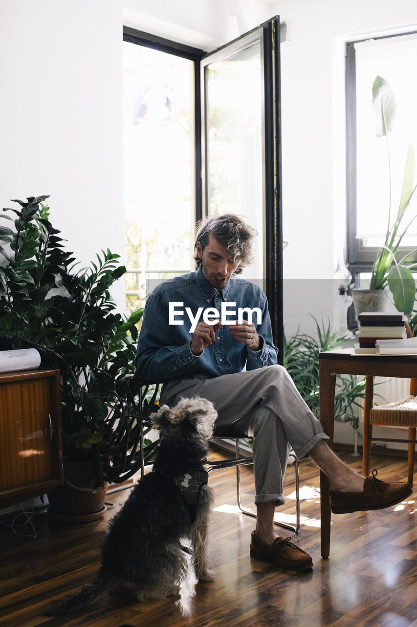 Full length of male architect talking with dog while sitting at home office