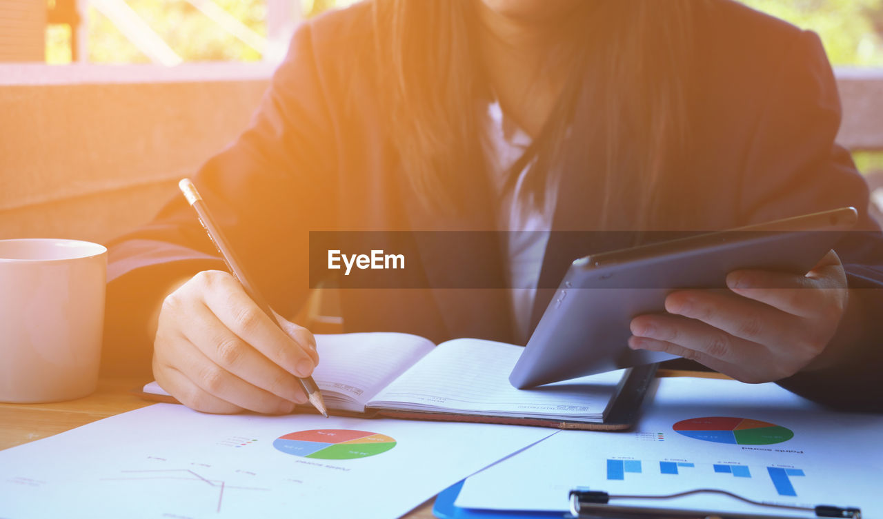 Midsection of businesswoman using digital tablet and analyzing paperwork on desk