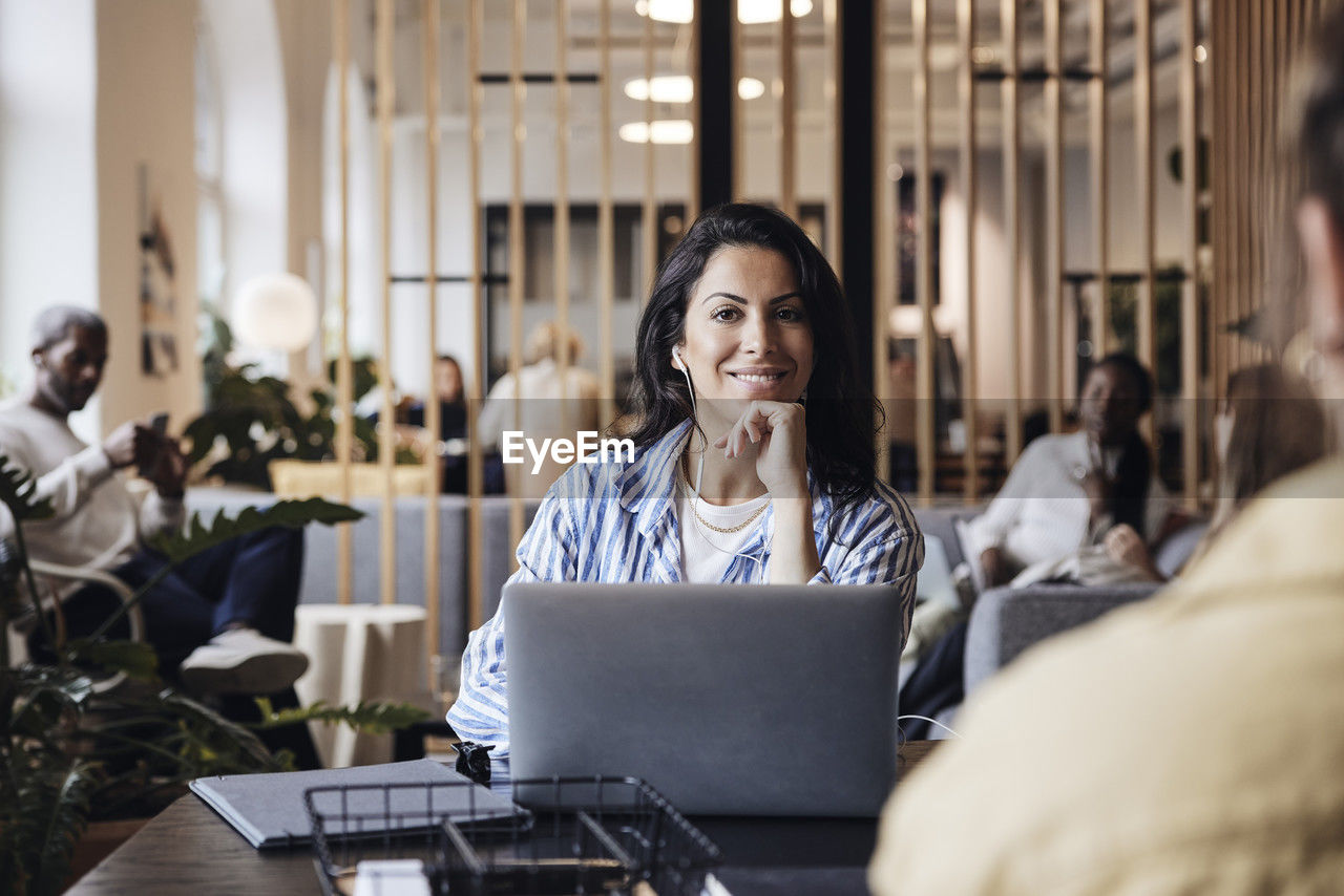 Portrait of smiling businesswoman sitting with hand on chin at coworking office