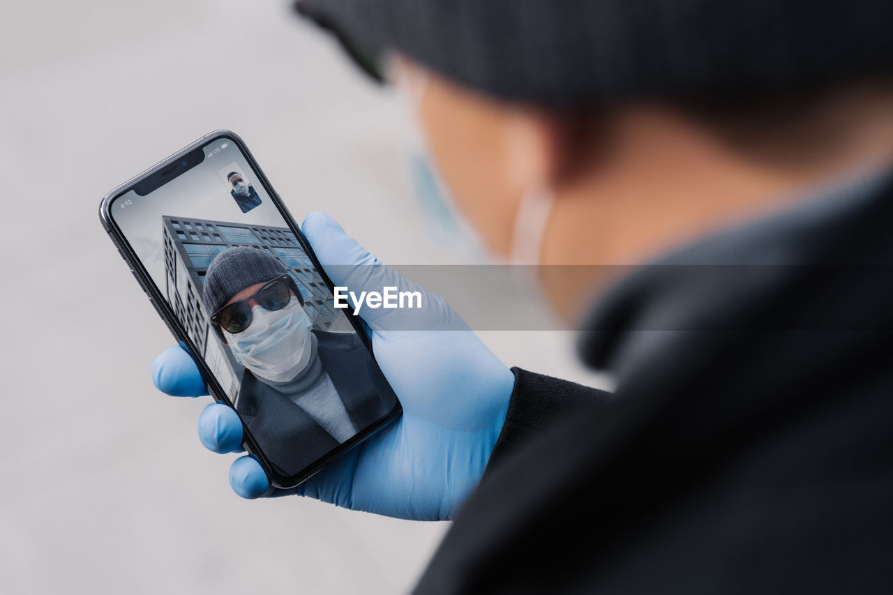 Midsection of man wearing mask video conferencing over mobile phone