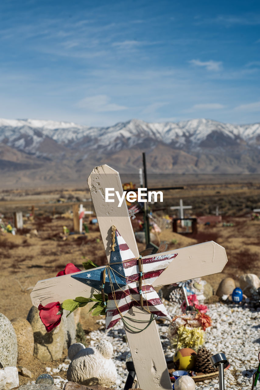 Wooden cross on grave in desert cemetery with distant snowy mountains