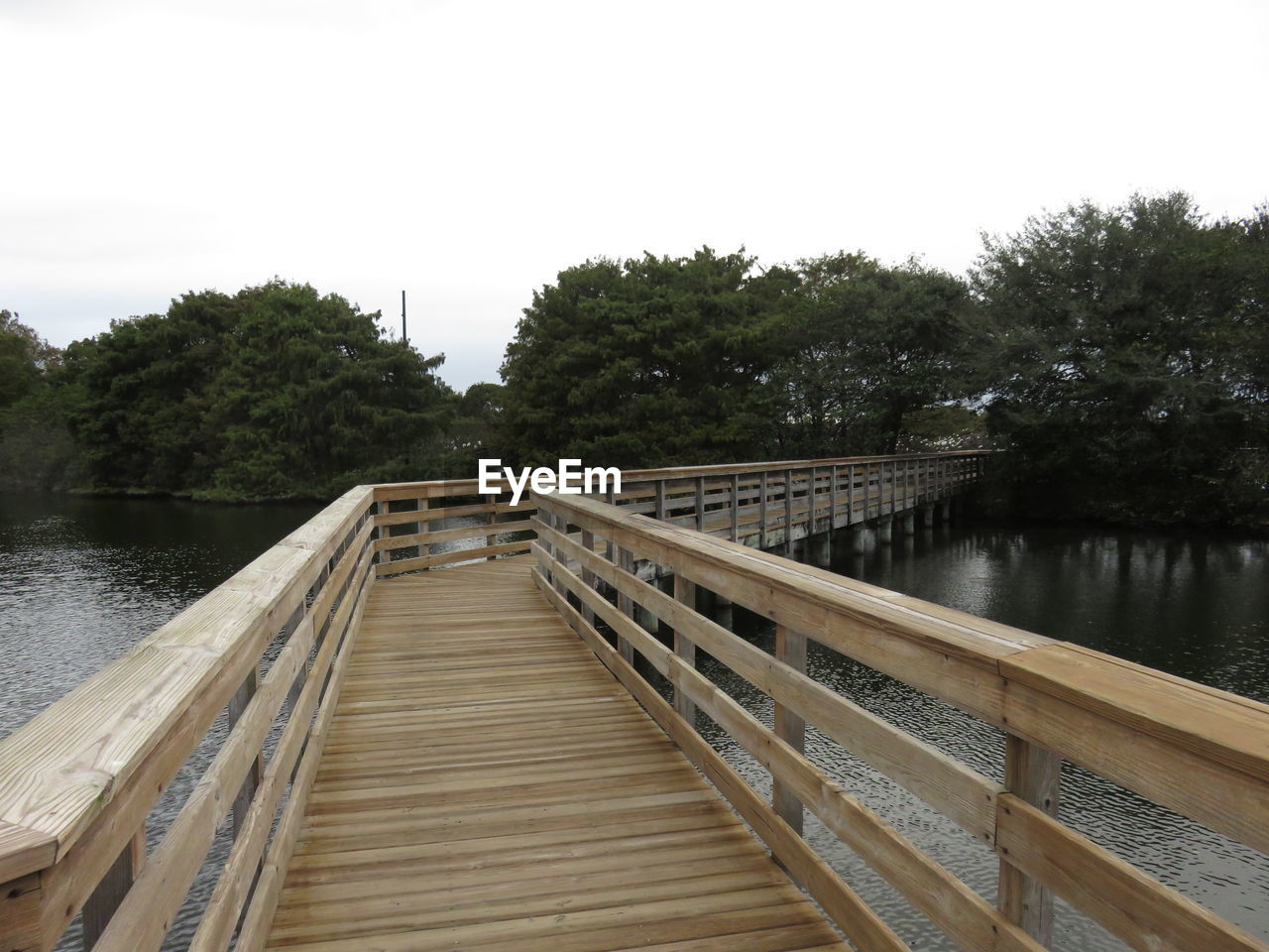 WOODEN FOOTBRIDGE OVER LAKE AGAINST SKY