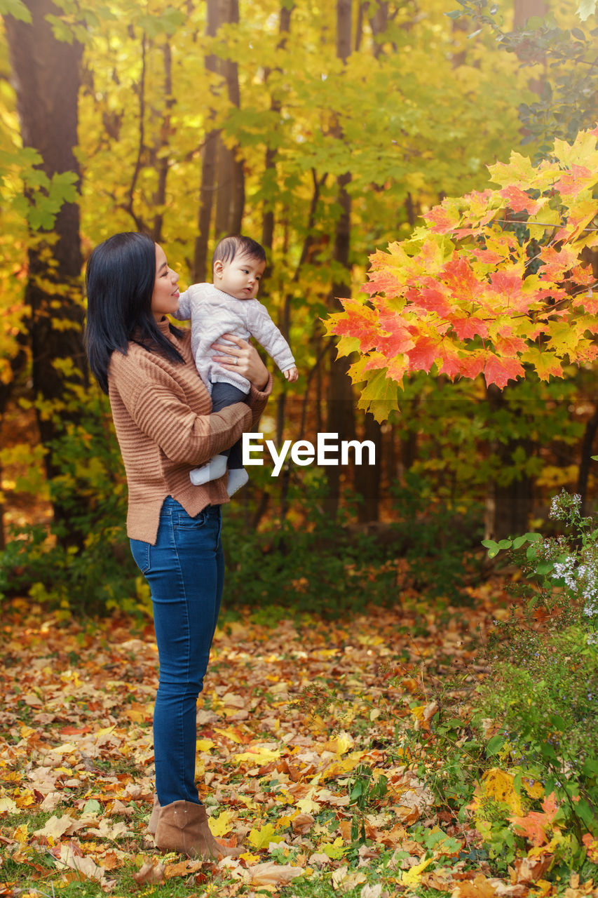 Mother carrying daughter while standing by tree during autumn