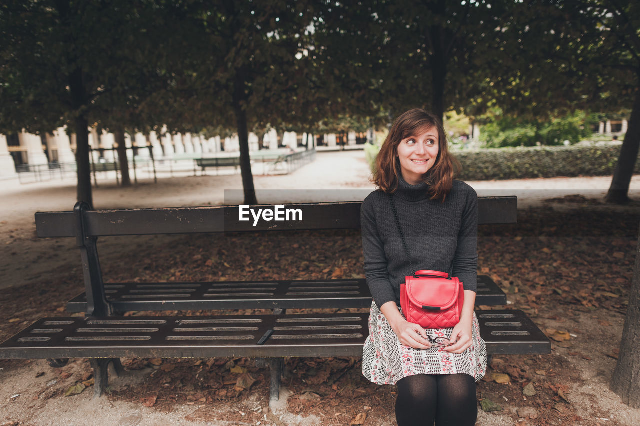 Young woman looking away while sitting on bench