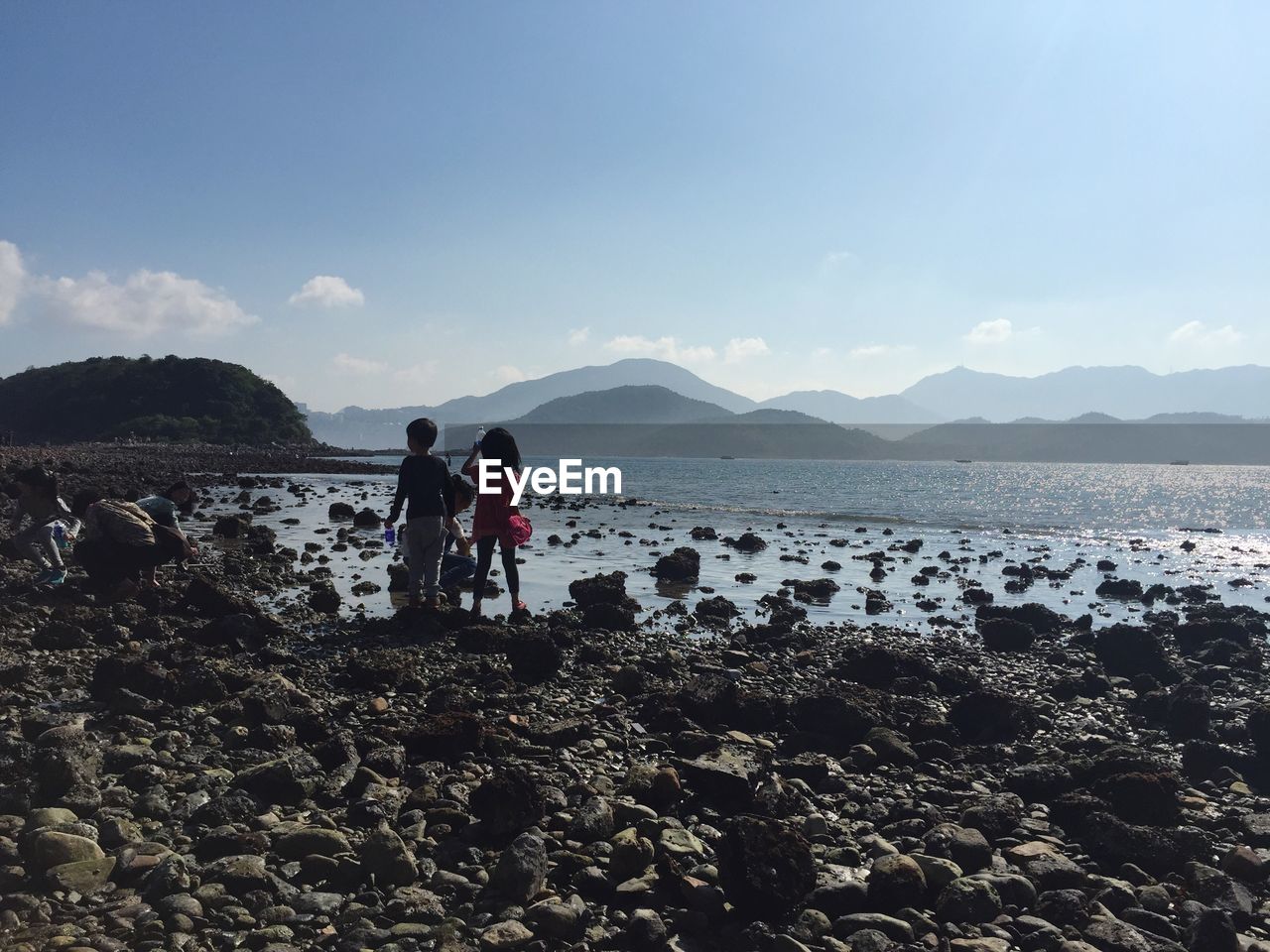 People on sea shore by mountains against sky