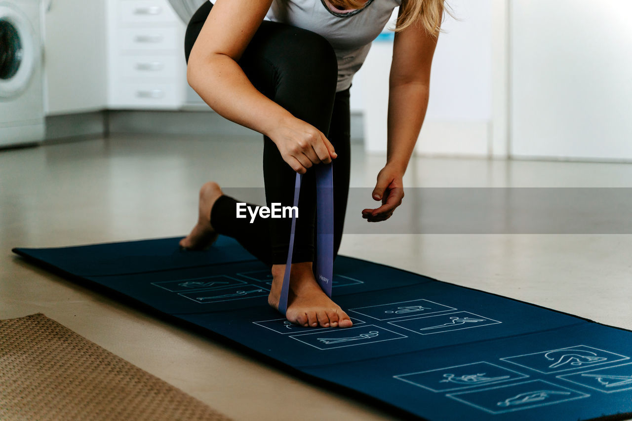 Cropped unrecognizable sportswoman in activewear performing arms exercise by using elastic band while working out on mat at home