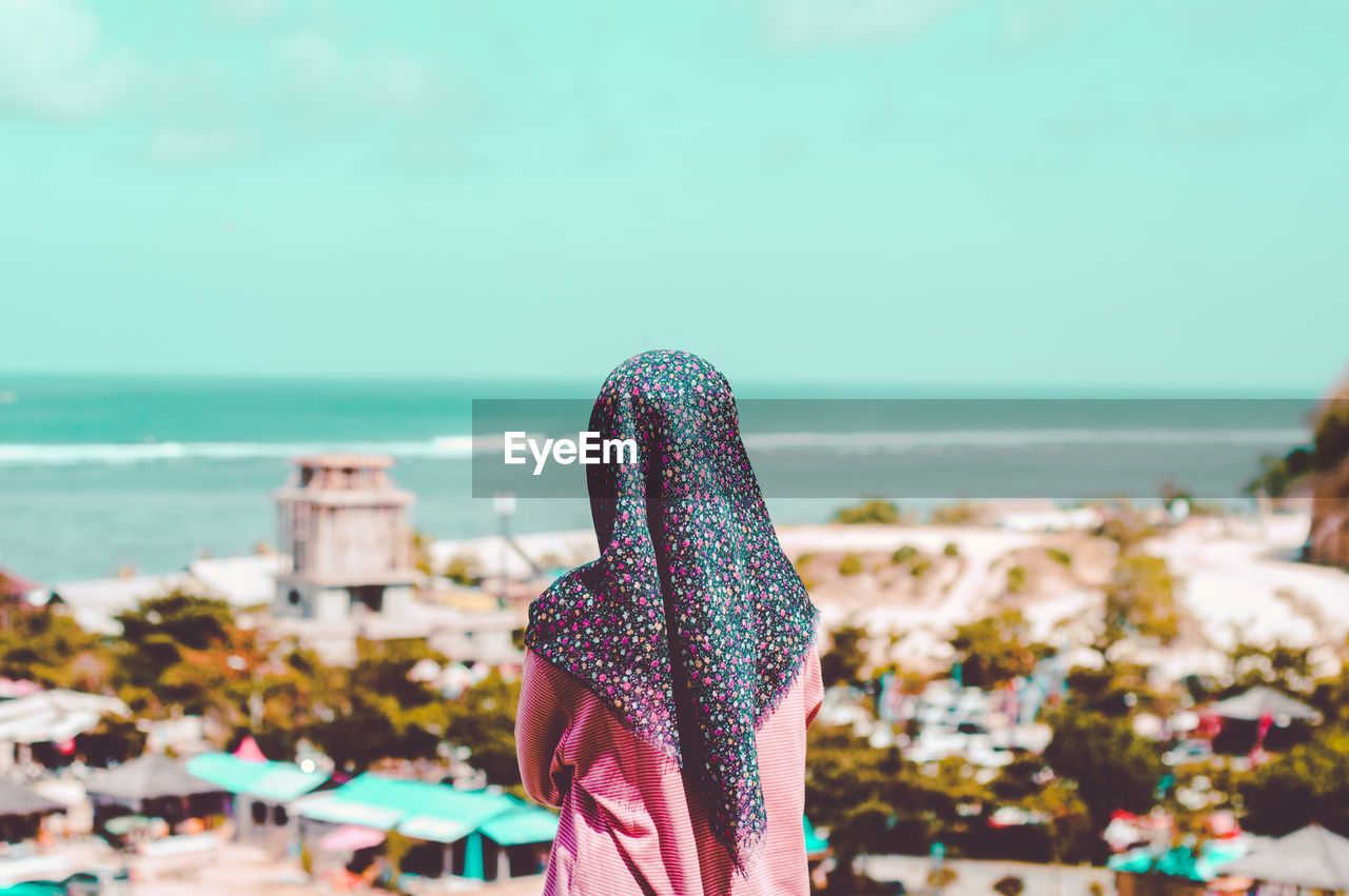 Rear view of woman wearing hijab looking at view while standing at beach