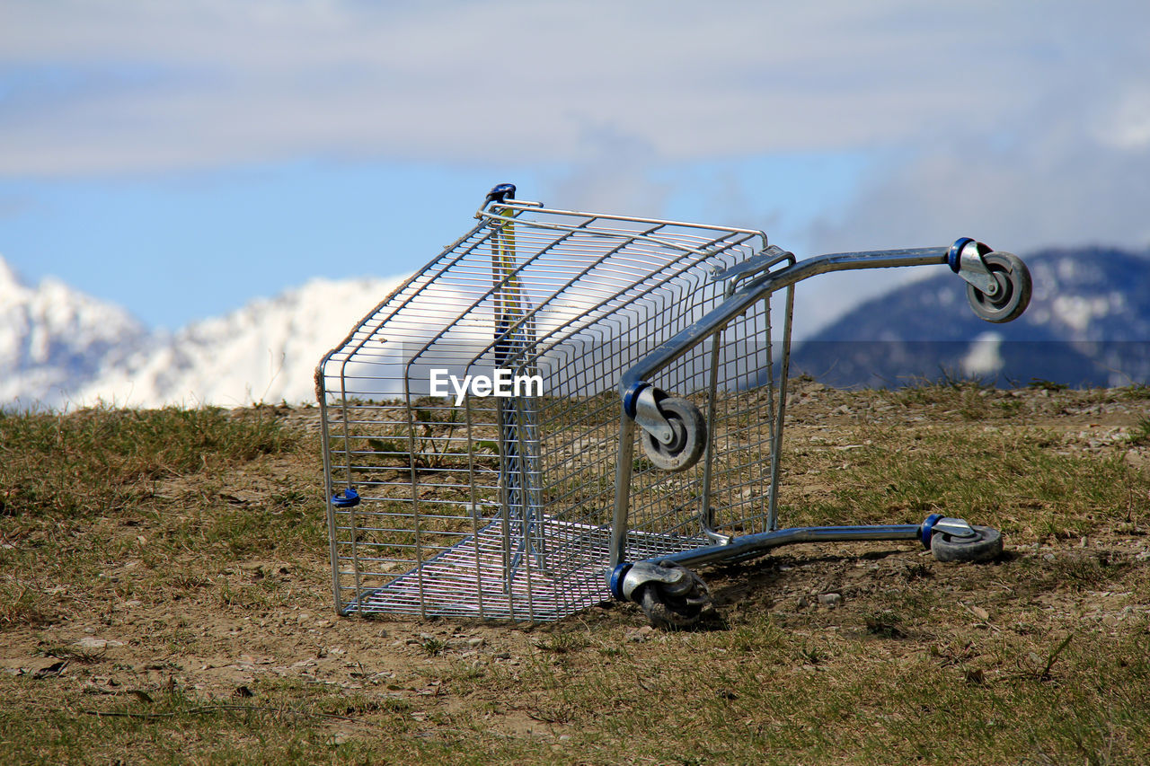 Close-up of shopping cart on field against sky