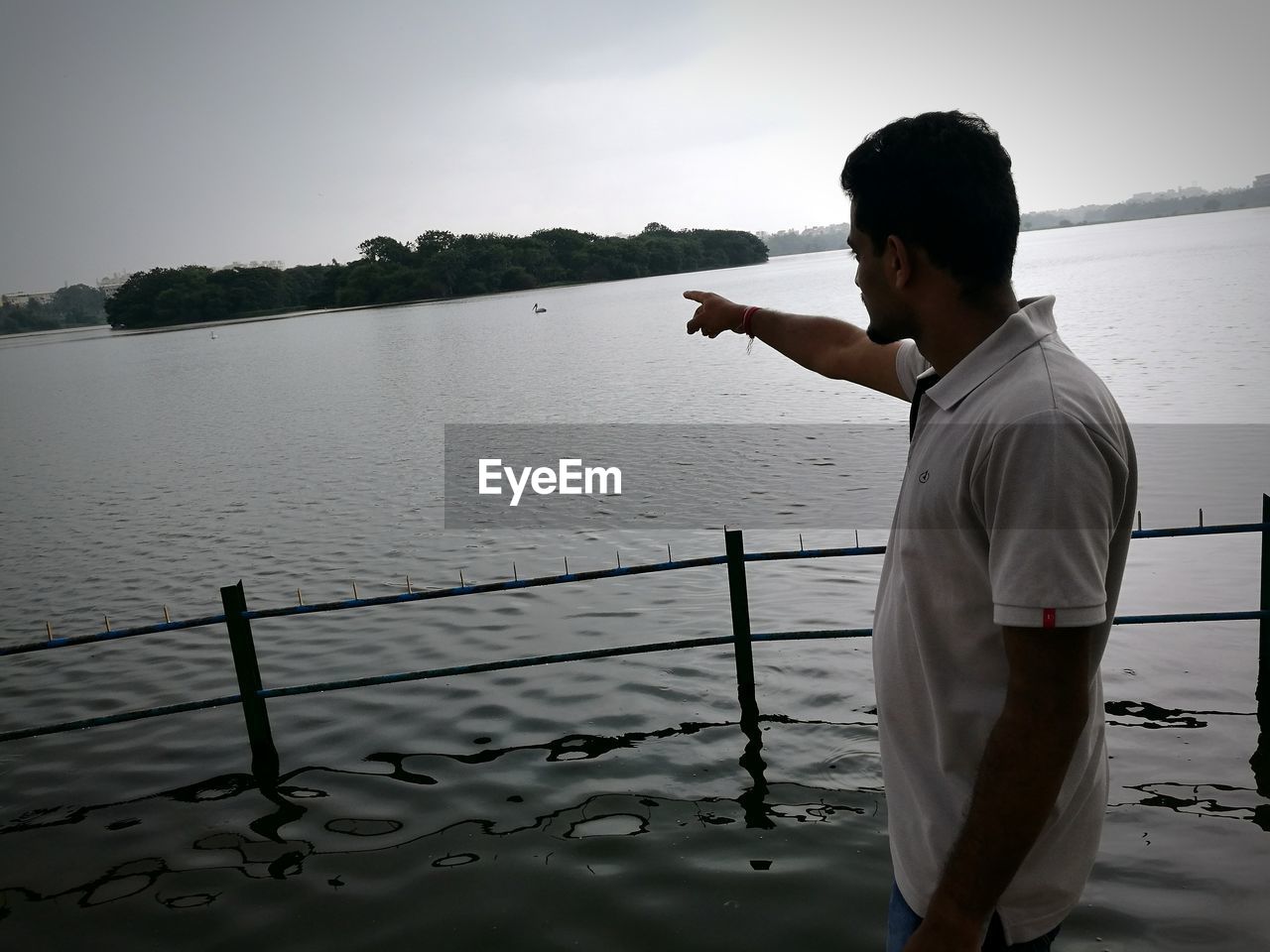 Side view of man pointing at lake against sky