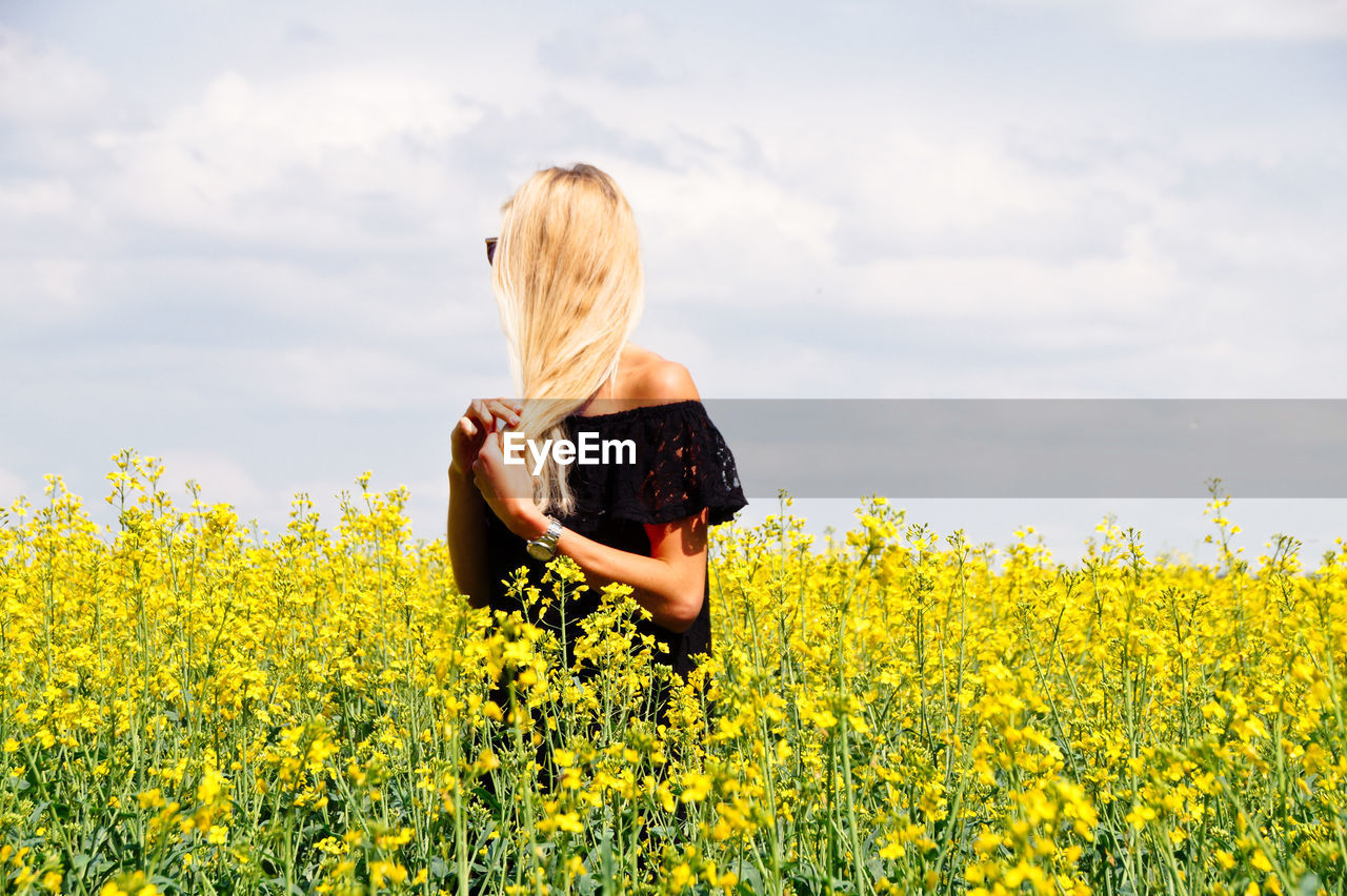 Young woman with hand in hair standing on oilseed rape field