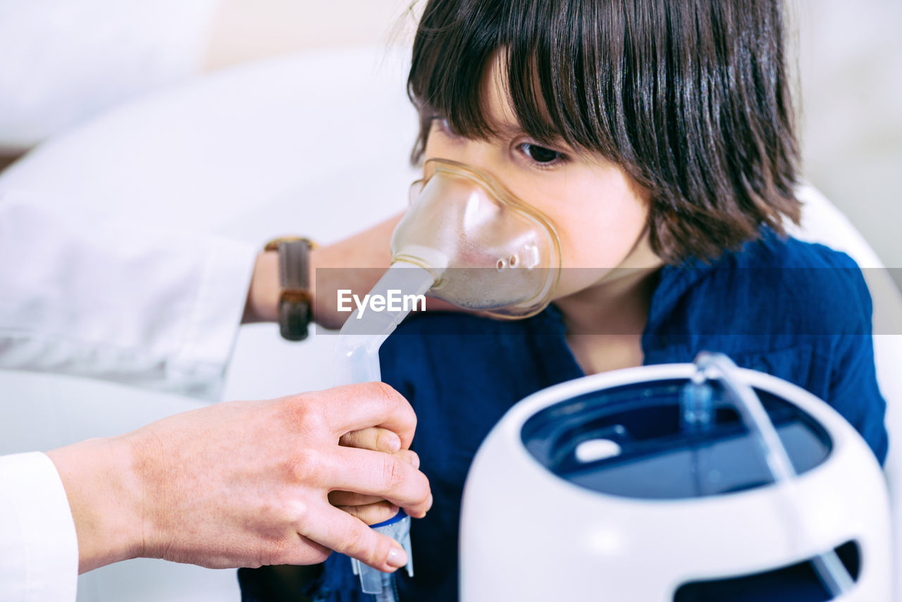 Cropped hand of female doctor holding oxygen mask on girl face in hospital