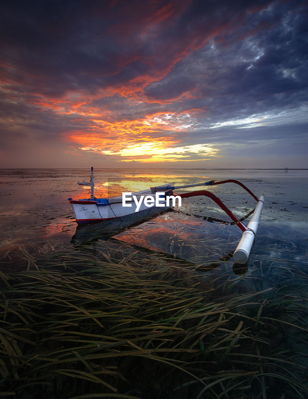 Boat moored on shore against sky during sunrise 